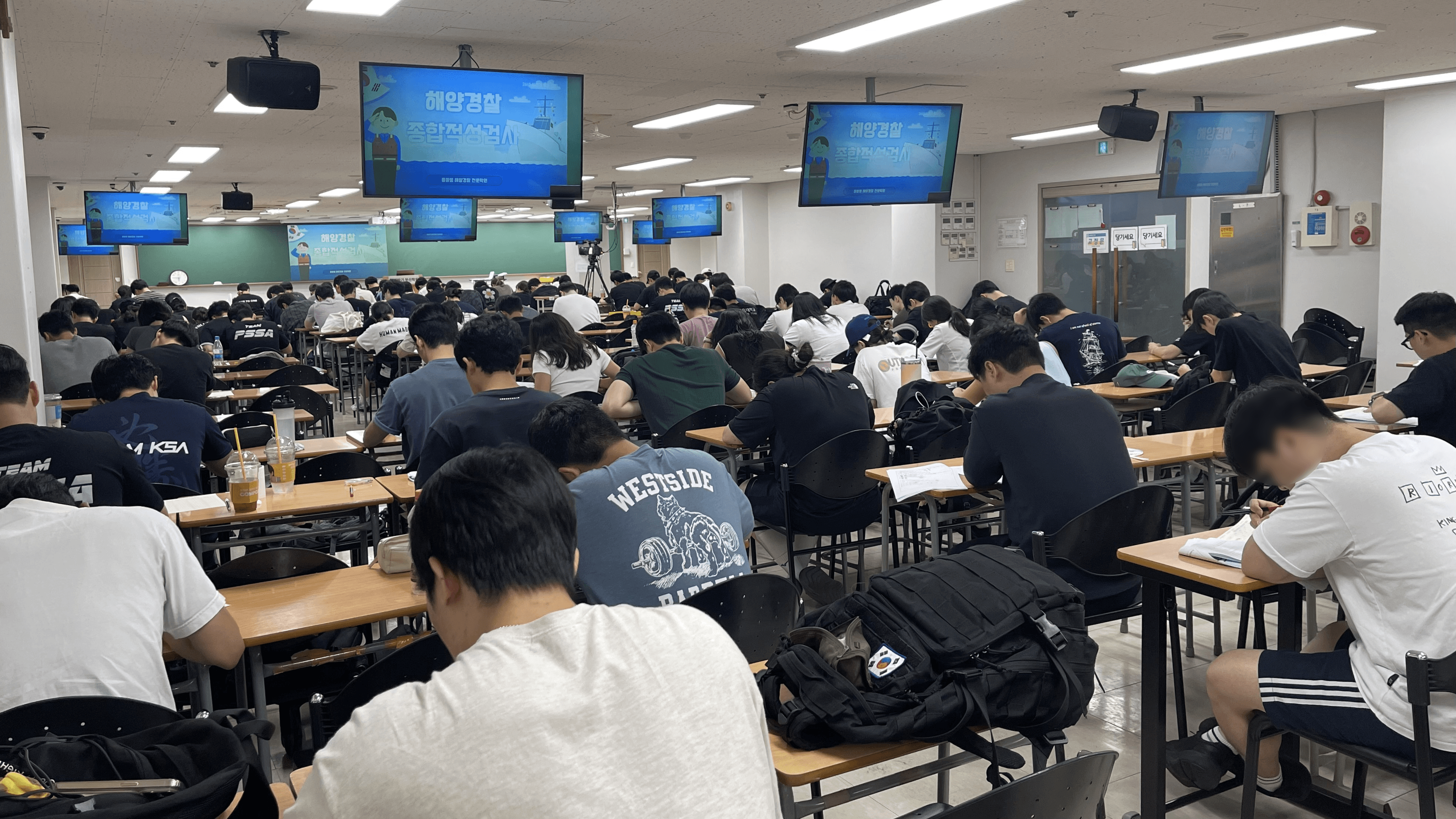 해양경찰 종합적성검사 화면이 켜진 큰 강의실에서 수강생들이 시험을 치르는 모습